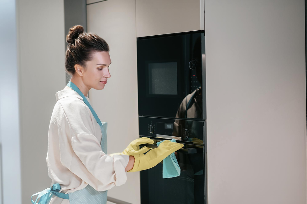 Vrouw in keuken maakt een zwarte inbouwoven schoon met gele handschoenen en blauwe doek; rustige, lichte sfeer
