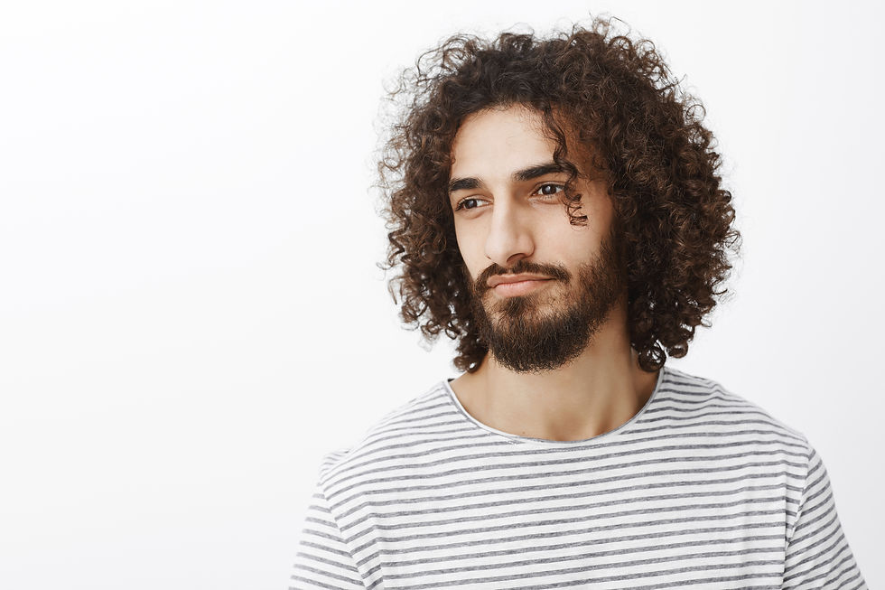 Een man met krullend haar en een baard kijkt naar links, gekleed in een gestreept shirt. Neutrale achtergrond, rustige uitstraling.