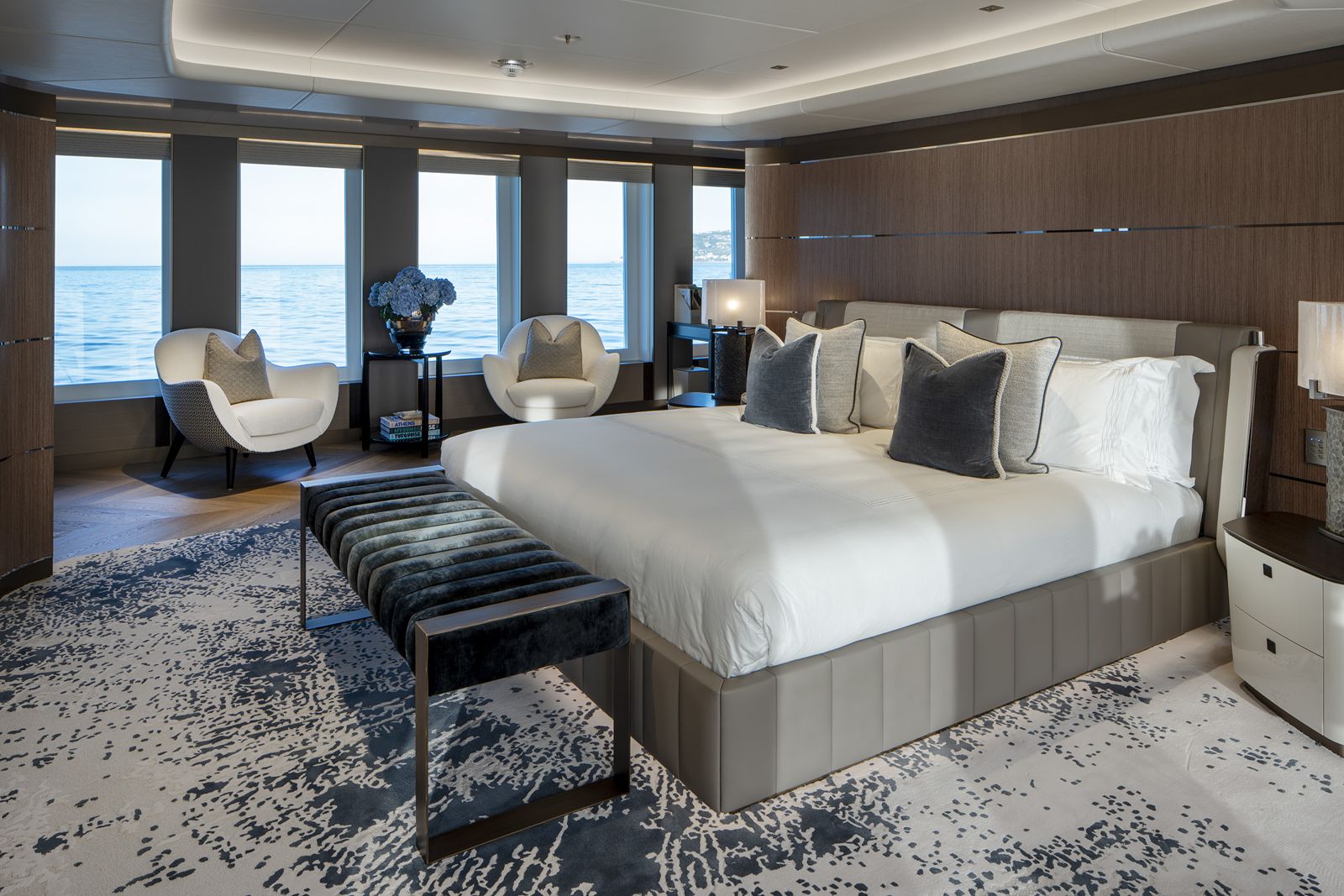 Yacht stateroom with a large bed, upholstered bench and armchairs facing the sea