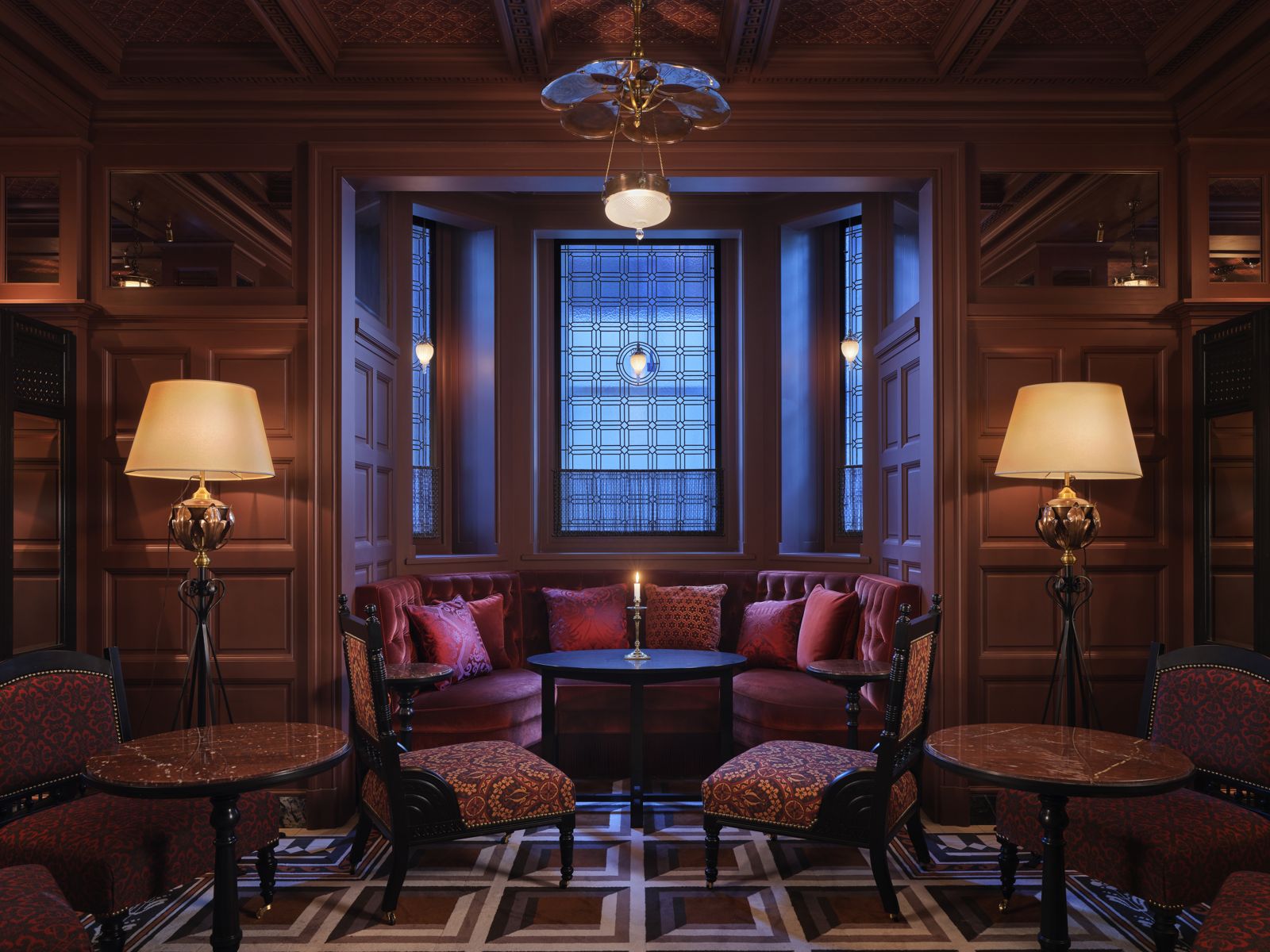 Panelled lounge in deep red, with a bay window, tapestry armchairs and two brass floor lamps