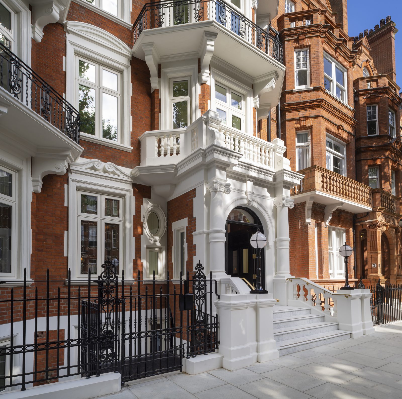 Red-brick mansion block with a white stone porch, marble steps and black iron railings, lit by globe lanterns on the entrance piers