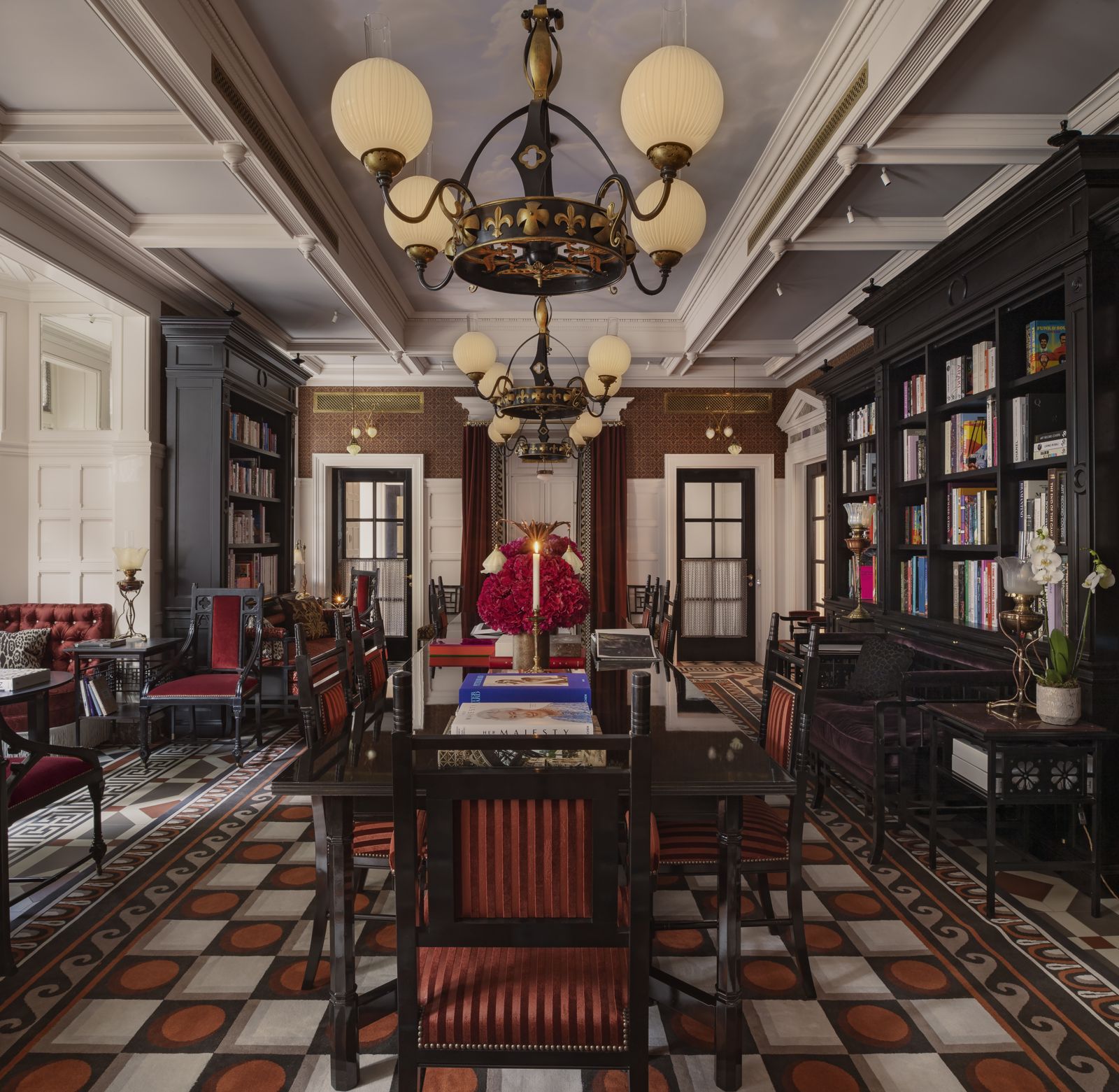 Library with black bookcases and two ornate iron and brass globe chandeliers over a long table
