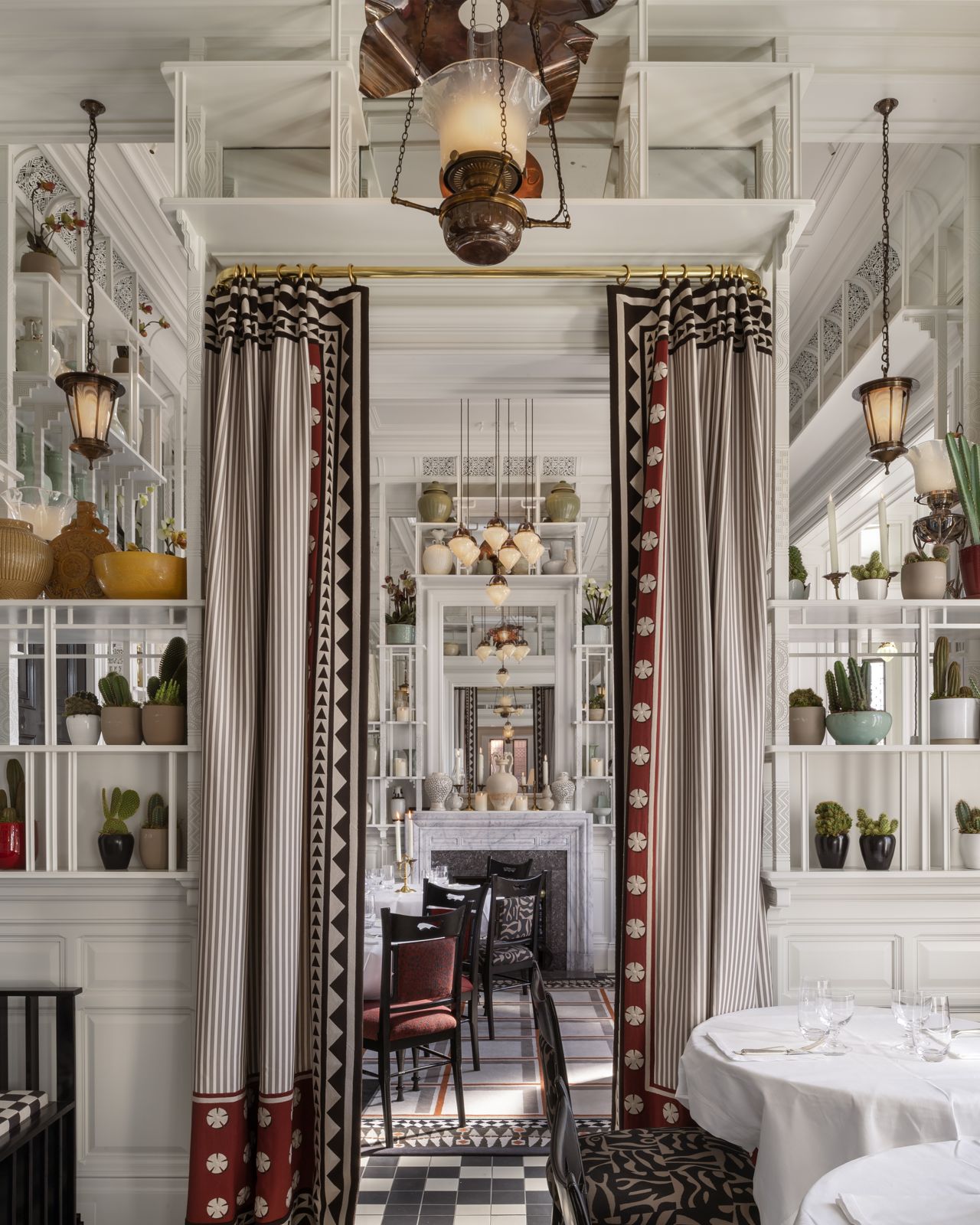White dining room seen through striped curtains, with lanterns and a hanging oil-lamp fitting
