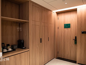 A hotel room entrance with a wooden door, closet, and a shelf holding a coffee machine, cups, and glassware