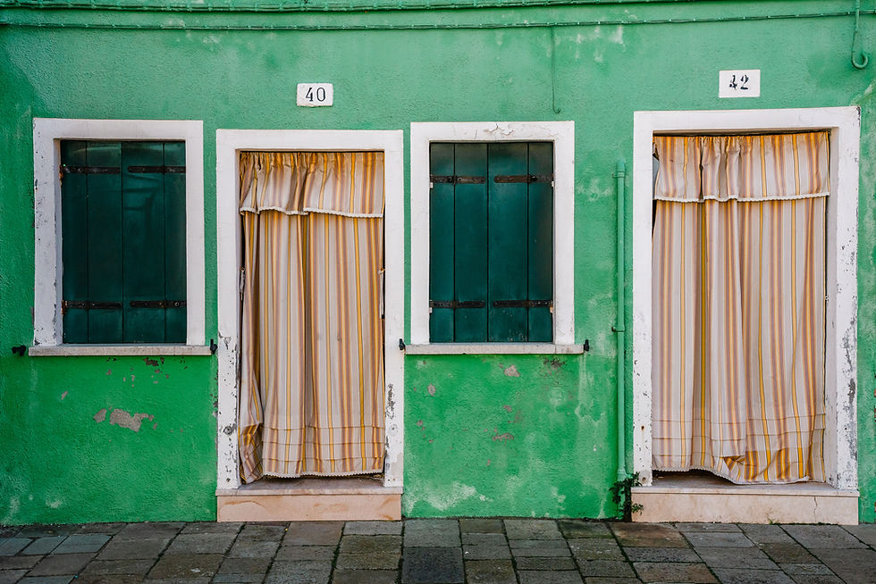 Photographie d’art d’une façade colorée typique de Burano avec volets verts et rideaux rayés.