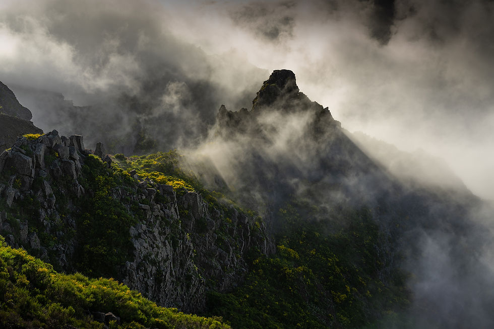 Paysage du Pico do Arieiro avec des rayons de lumière traversant les nuages et illuminant les pentes verdoyantes.