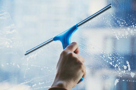 Close-up of a janitorial professional using a squeegee on the inside of an exterior office window.