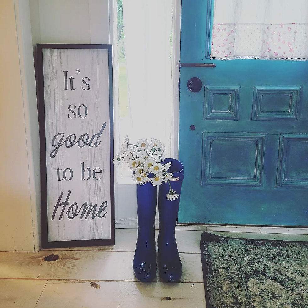 Cozy home entryway with a teal door, blue rain boots holding white daisies, and a sign that reads 'It's so good to be Home', square image.