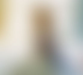 A person in a hospital bed gazes out a sunny window. The room is bright with white bedding and a light blue wall, creating a calm mood.