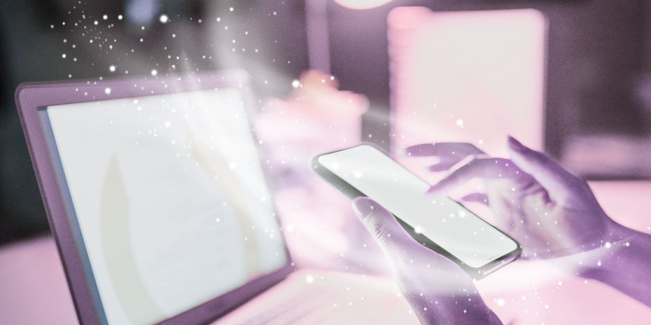 Hands holding a glowing smartphone in front of a laptop, surrounded by sparkles. The scene has a magical, futuristic feel with pink hues.