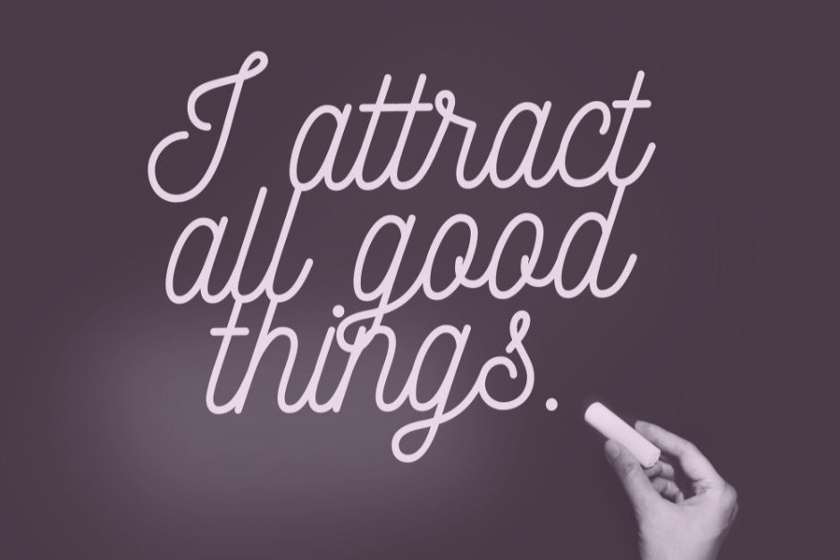 Hand holds chalk writing "I attract all good things" on a purple background, conveying positivity and inspiration.