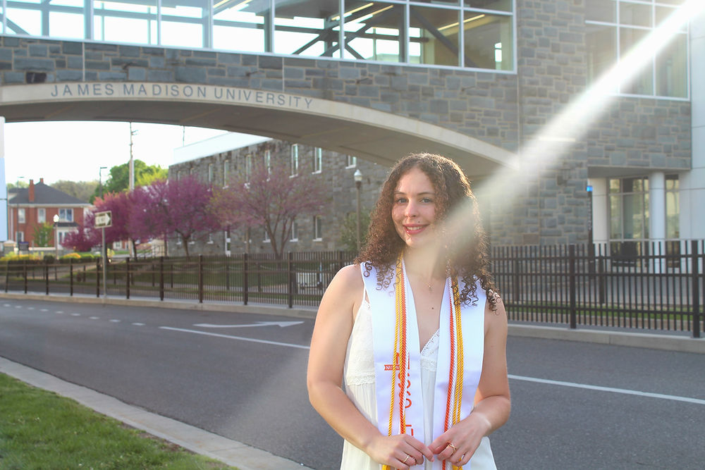 A JMU grad smiling by the Skybridge by the SSC on campus