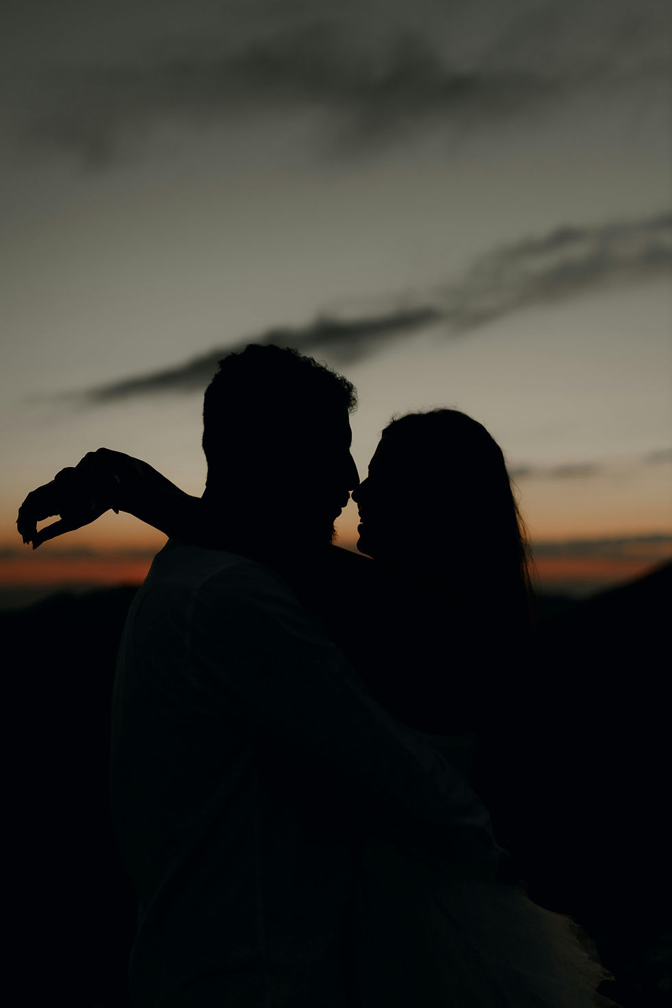 Silhouet van een stel dat elkaar omarmt bij zonsondergang met een kleurrijke lucht als achtergrond, uitstralend liefde en intimiteit.