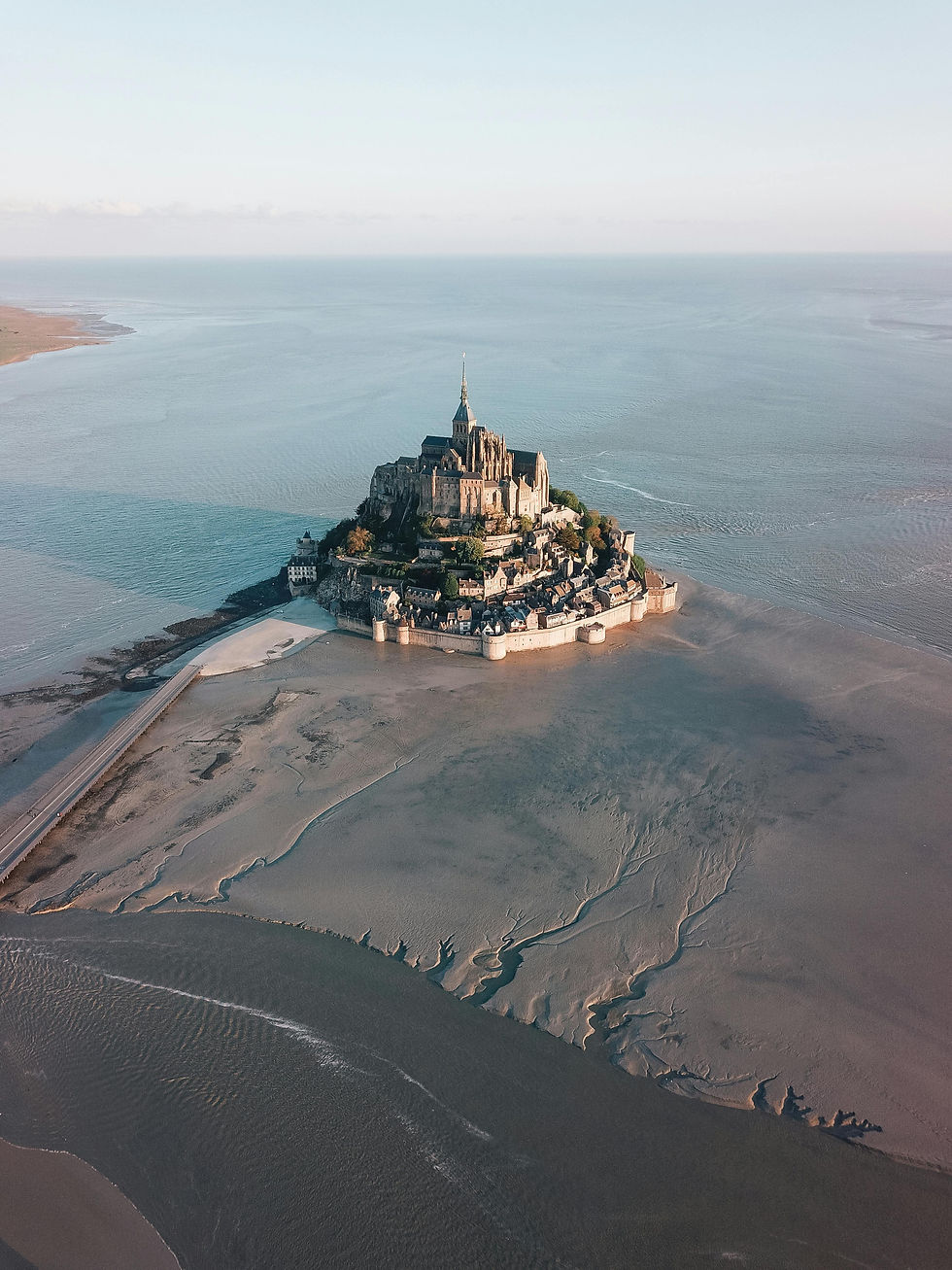 Mont Saint-Michel tijdens eb, omringd door zand en water. Het eilandje met gebouwen en een abdij steekt statig boven de horizon uit.