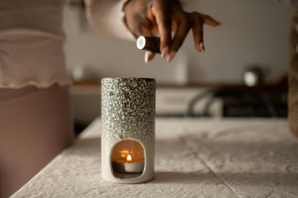 Hand druppelt olie in een grijze, gespikkelde geurbrander met een brandend kaarsje op een beige tafel. Rustige, sfeervolle keuken.