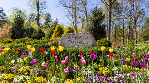 Asheville Cottages stone sign with colorful flowers in front of a garden.