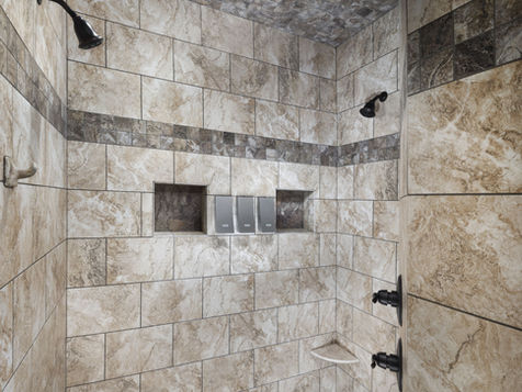 Tiled shower with showerheads and built-in shelves featuring soap bottles.