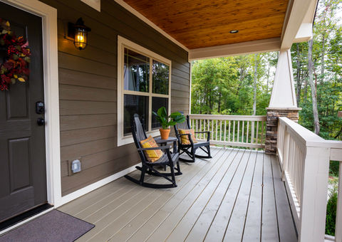 Front porch with rocking chairs and door, wooden floor and railing.