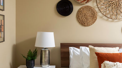 Bedroom with decorative wall hangings, lamp, nightstand, and bed with pillows.