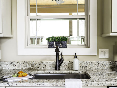 Kitchen sink with black faucet, window, white cabinets, and granite countertop.