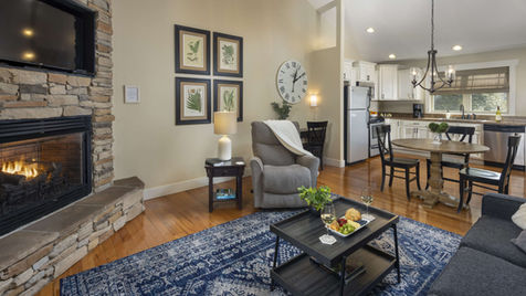 Cozy living room with fireplace, white walls, clock, and dining area Asheville Cottages New Site