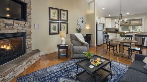 Cozy living room with fireplace, white walls, clock, and dining area Asheville Cottages New Site