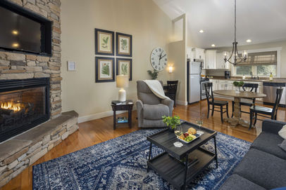 Cozy living room with fireplace, white walls, clock, and dining area Asheville Cottages New Site