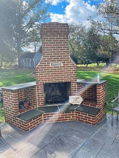 Outdoor fireplace with chimney. Small stone patio with herringbone pattern; rectangle stone pavers laid perpendicular to each other creating a flat walking surface.