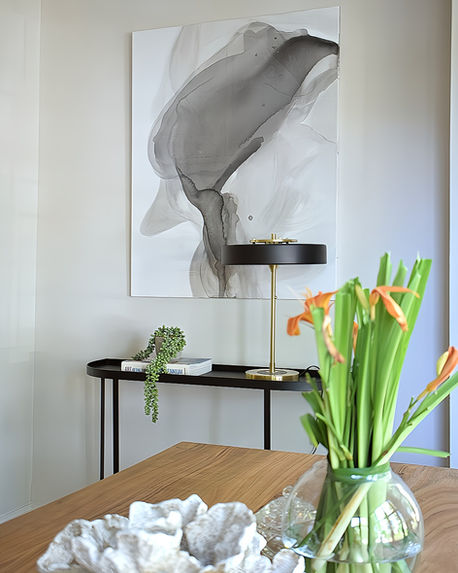 Styled vignette featuring wooden dining table, fresh tulips in glass vase, and abstract wall art in a soft neutral interior.