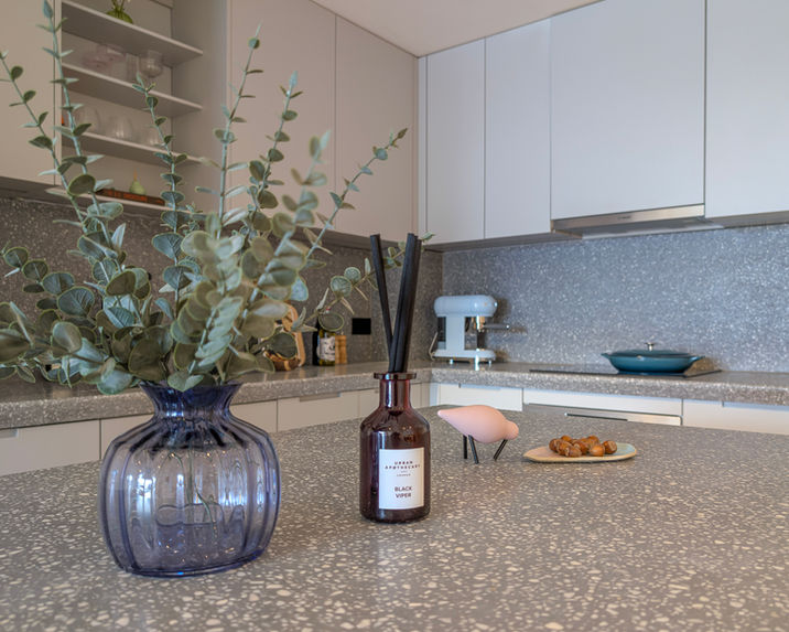 Close-up of terrazzo kitchen worktop styled with blue glass vase, eucalyptus stems and designer candle in luxury apartment staging.