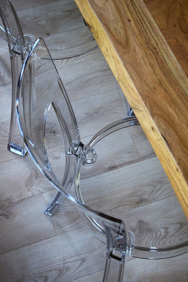 Overhead detail of transparent acrylic dining chair placed on light wood flooring beside a solid oak dining table.