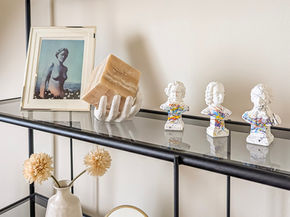 Shelf styling detail featuring framed art, sculptural objects, and decorative accents arranged on a sleek black display table in a Victorian-era interior.