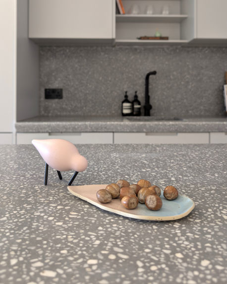 Terrazzo kitchen island with neutral cabinetry and styled ceramic décor in contemporary London apartment.
