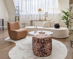 Bright modern living area with circular sofa, textured accent chair and statement ottoman in premium city apartment