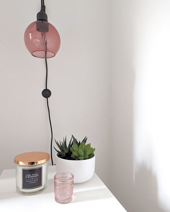 Close-up of pink pendant light above bedside table with candles and plant.