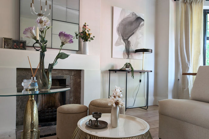 Fireplace focal point with abstract artwork above, velvet sofa, layered textiles, and gold-toned decorative accents in a classic interior setting.