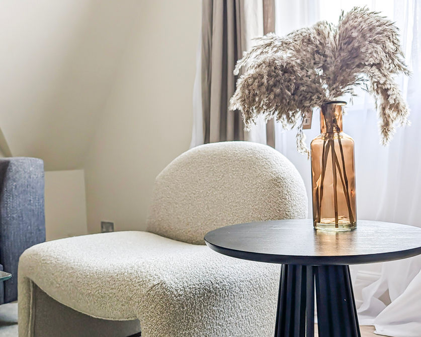 Amber glass vase with pampas arrangement on a round black side table beside textured boucle armchair in a period reception room.