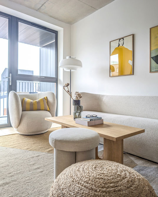 Contemporary living room with neutral curved sofa, light wood coffee table and abstract yellow wall art in bright London flat.