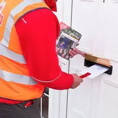Royal Mail postal worker delivering mail and flyers into a letterbox.