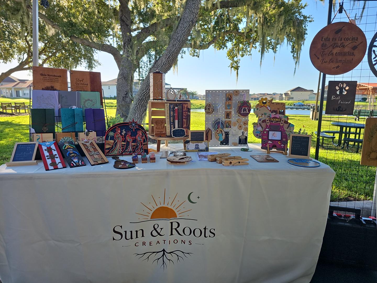 Our Sun & Roots Creations market display with handmade products and our logo on the tablecloth