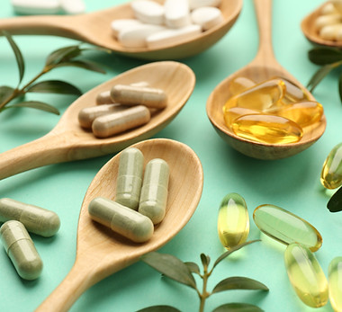 Different vitamin capsules in spoons and leaves on turquoise background, closeup