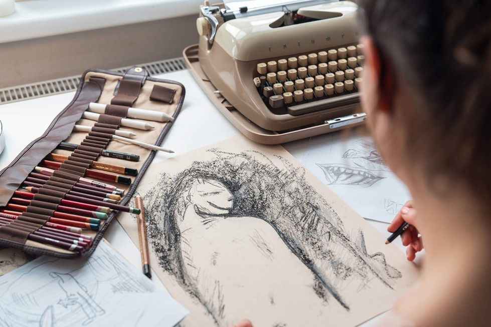Nahaufnahme eines Schreibtisches, auf dem verschiedene Zeichenmaterialien wie Bleistifte und Kreiden in einem Etui, eine Skizze einer Figur auf braunem Papier und eine Schreibmaschine liegen. Im Vordergrund zeichnet eine Person an der Skizze. Die Szene zeigt eine kreative Arbeitsumgebung mit künstlerischen Werkzeugen und Entwürfen.