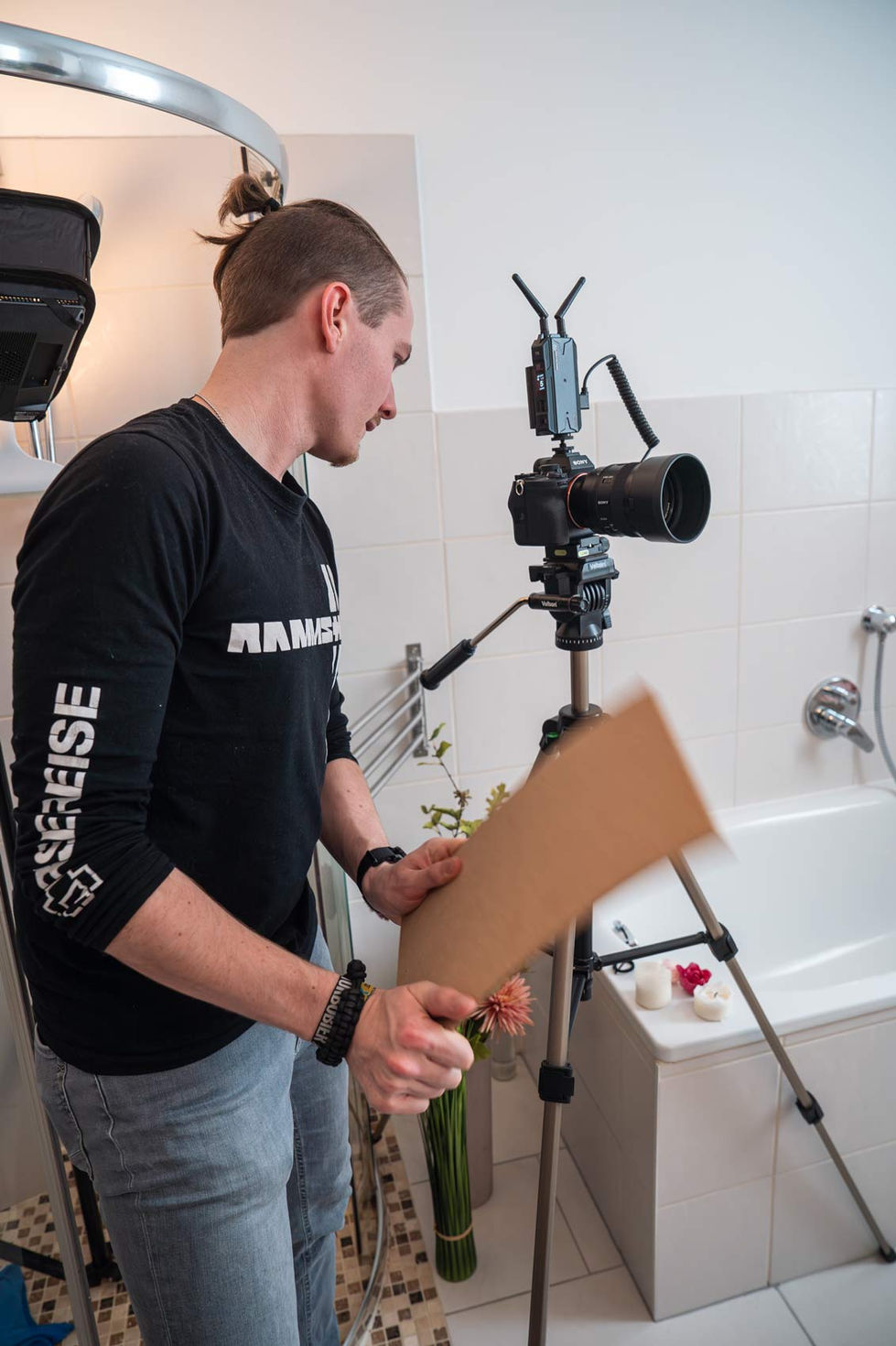 Ein Mann bereitet eine Kamera auf einem Stativ im Badezimmer vor und hält eine braune Karte in der Hand.