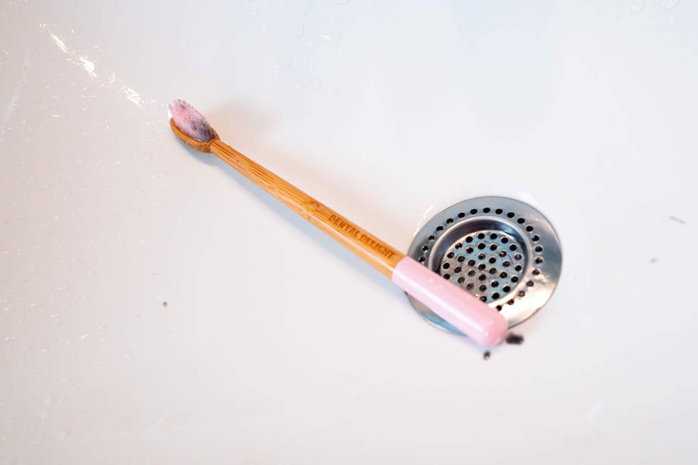 Eine Zahnbürste aus Bambus mit einem rosa Griff liegt in einem weißen Waschbecken neben dem Abfluss. Die Zahnbürste hat Zahnp