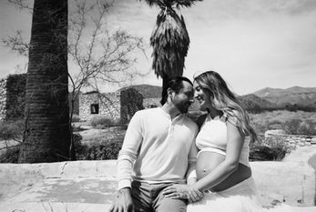 Couple sitting together during maternity session at Mission Creek Preserve, black and white film photo in the High Desert near Joshua Tree