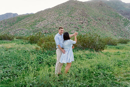 Couple dancing together among lush spring desert greenery beneath the rugged San Jacinto Mountains during a Palm Springs family session at Ship Rock.