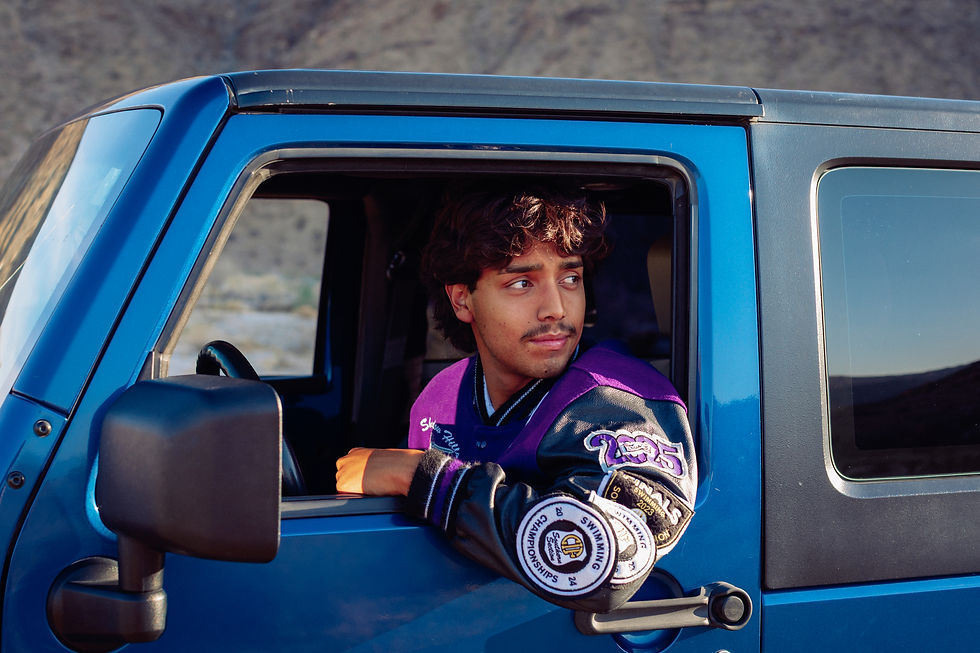 Smiling high school graduate sitting inside his blue Jeep Wrangler during senior portrait session. Palm Springs senior photographer capturing joyful, candid moment.
