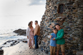 Parents kissing at the base of Pirate Tower in Laguna Beach while kids smile at the camera. Colorful rocks and ocean waves create a dreamy backdrop.