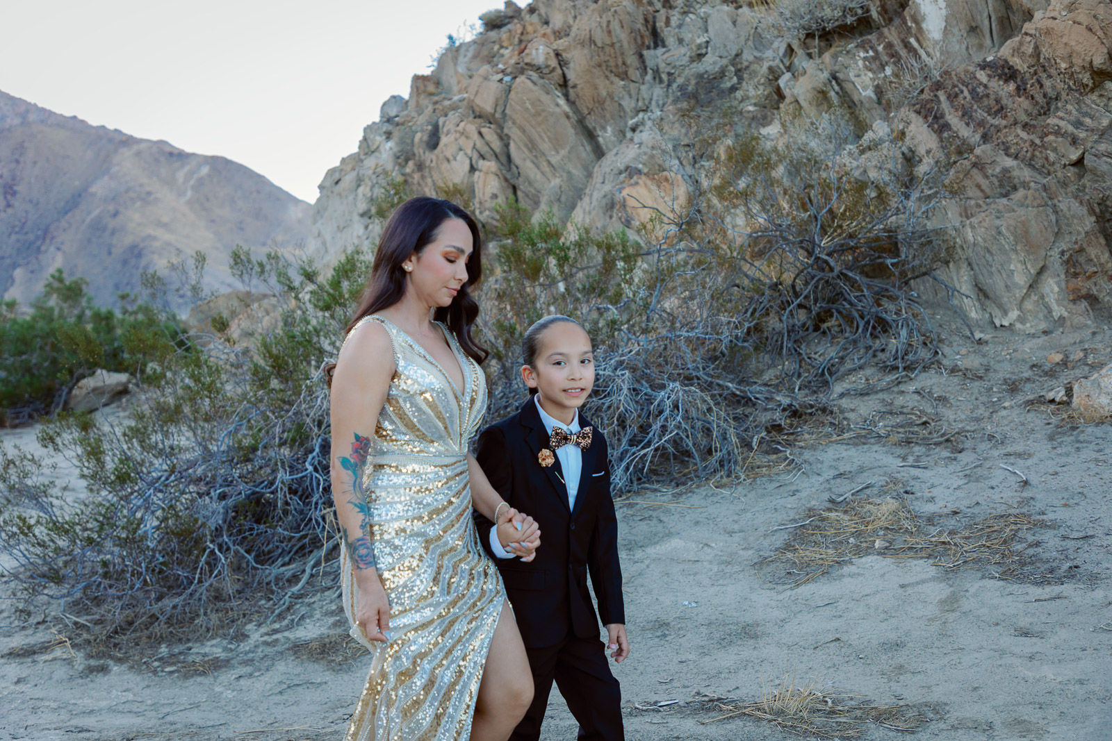 Mother and child dressed in formal attire walking together in the desert during a Joshua Tree family photography session
