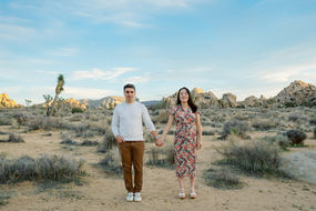 Couple holding hands in Joshua Tree desert during maternity session with mountains and Joshua trees in background.